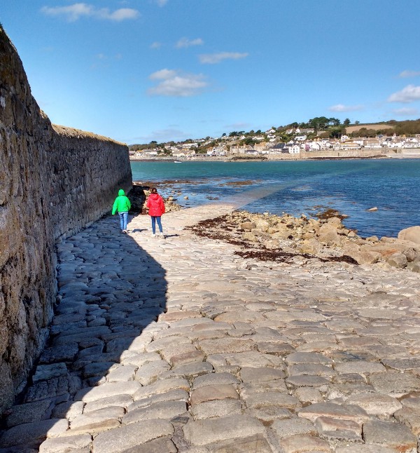 It shows two children on a cobbled road that disappears into the sea. It shows how a road can be difficult to follow.